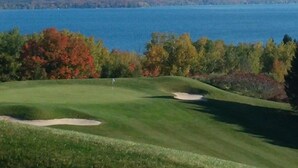 A golf course with a water body in the background. - Torch lake waterfront:100 ft of sandy beach, 3-bedroom, 3-bath cottage (Alden)