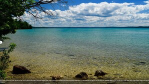 A clear view of Torch Lake with visible shoreline and rocks. - Torch lake waterfront:100 ft of sandy beach, 3-bedroom, 3-bath cottage (Alden)