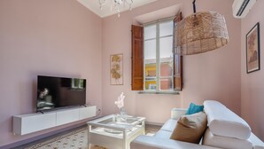 Sala de estar com televisão de tela plana, sofá branco e mesa de centro.