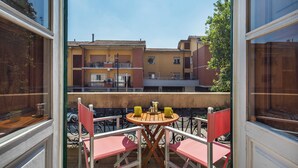 Uma varanda com mesa e cadeiras, com vista para um edifício com várias varandas e janelas.