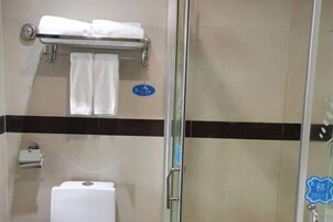 Un baño con cabina de ducha de vidrio, un perchero con toallas dobladas, un inodoro y un cartel azul en la pared.