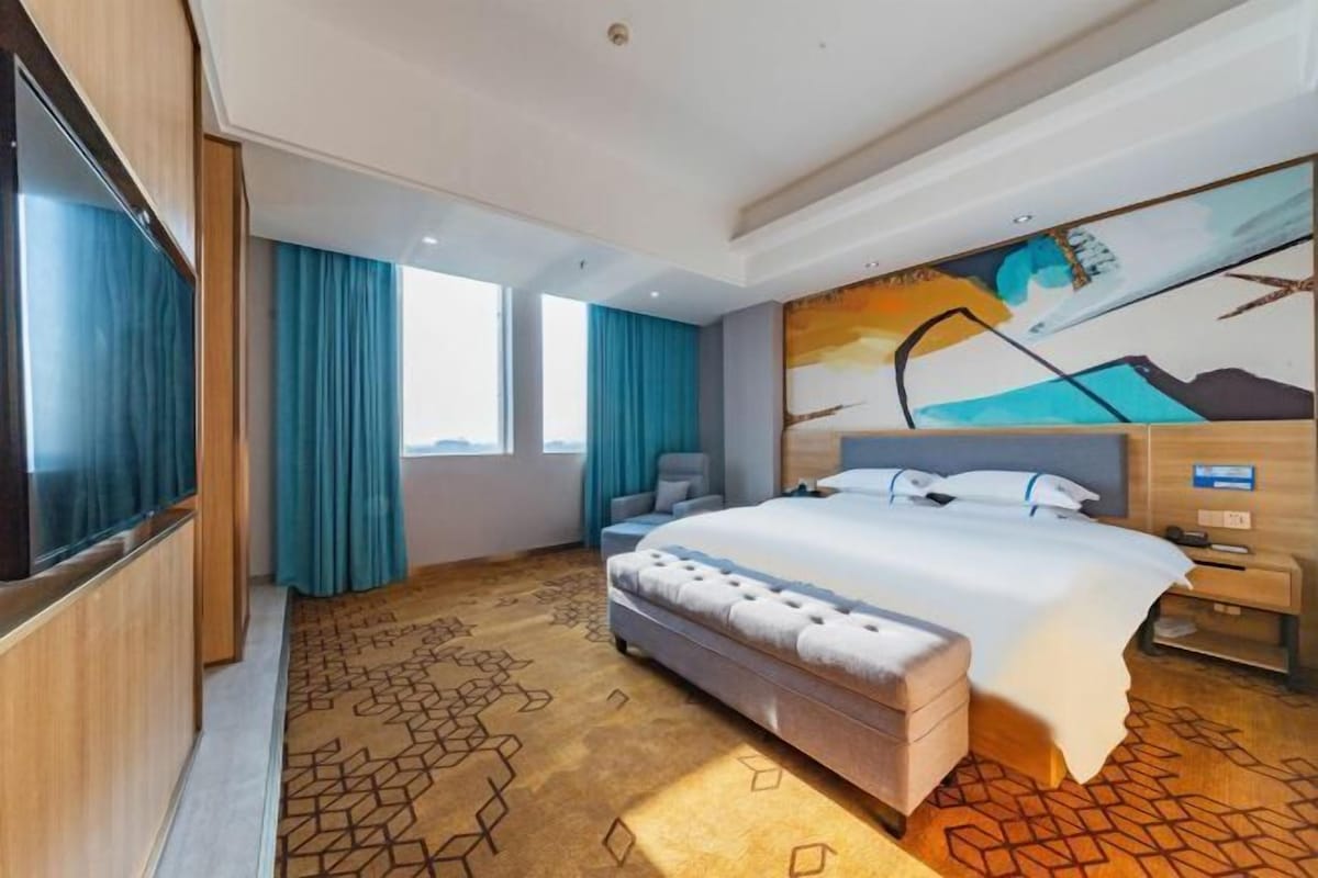 A hotel room with a large bed, a TV, a desk, and a painting on the wall.