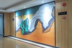 A modern hotel lobby with a large abstract mural on the wall, a wooden panel design, and a fire alarm on the right.