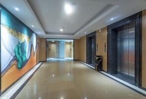 A hotel corridor with a polished floor, a mural on the left wall, and an elevator on the right.