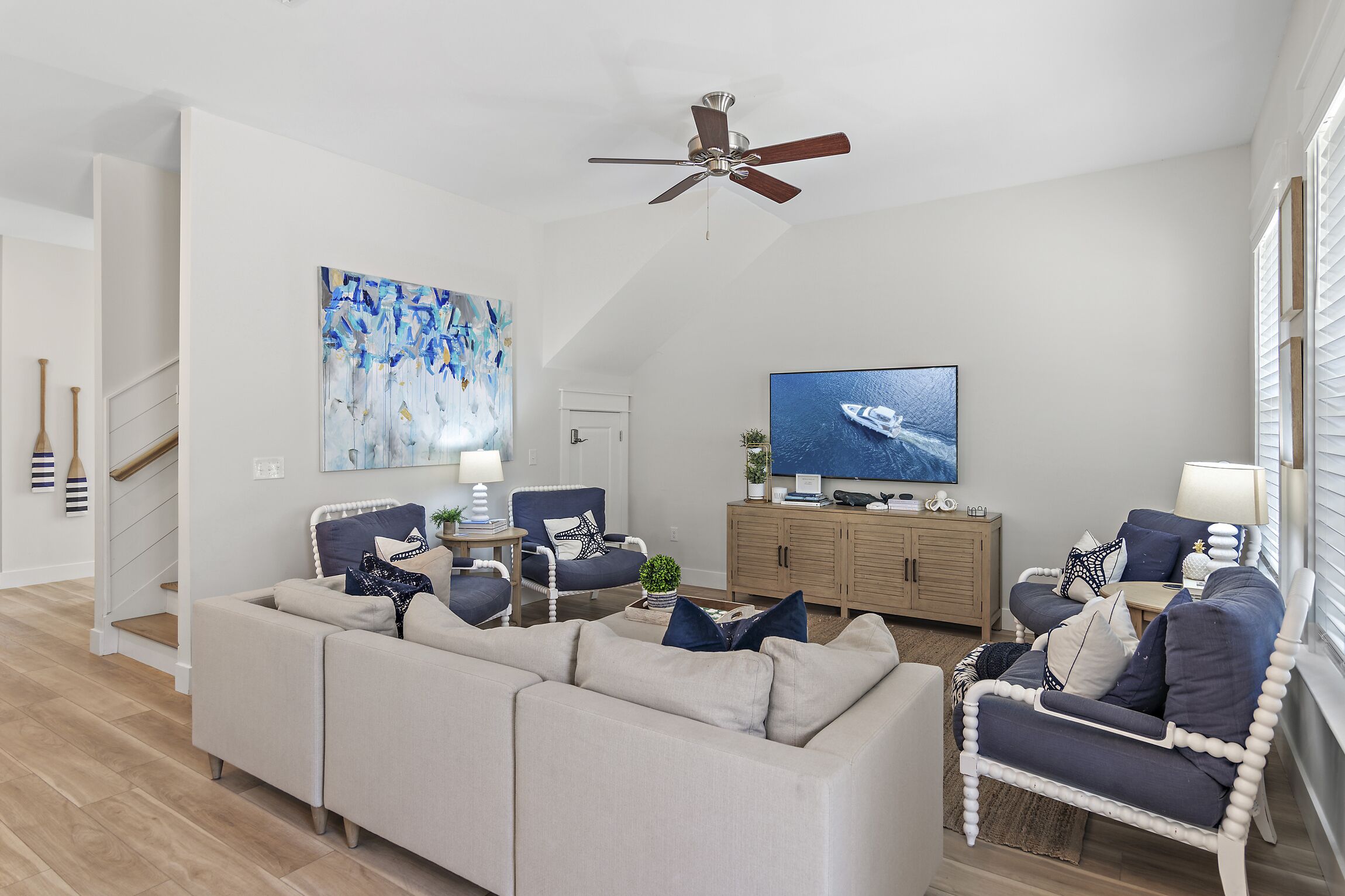 Un salon moderne avec un canapé d’angle, un fauteuil bleu, un meuble en bois et un ventilateur de plafond.
