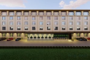 Un hôtel à plusieurs étages, doté d’une façade uniforme, d’une entrée centrale avec un escalier et d’un parking où sont stationnées plusieurs voitures.