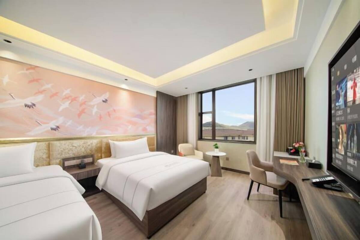 A hotel room with two beds, a desk, a TV, and a large window with a view.
