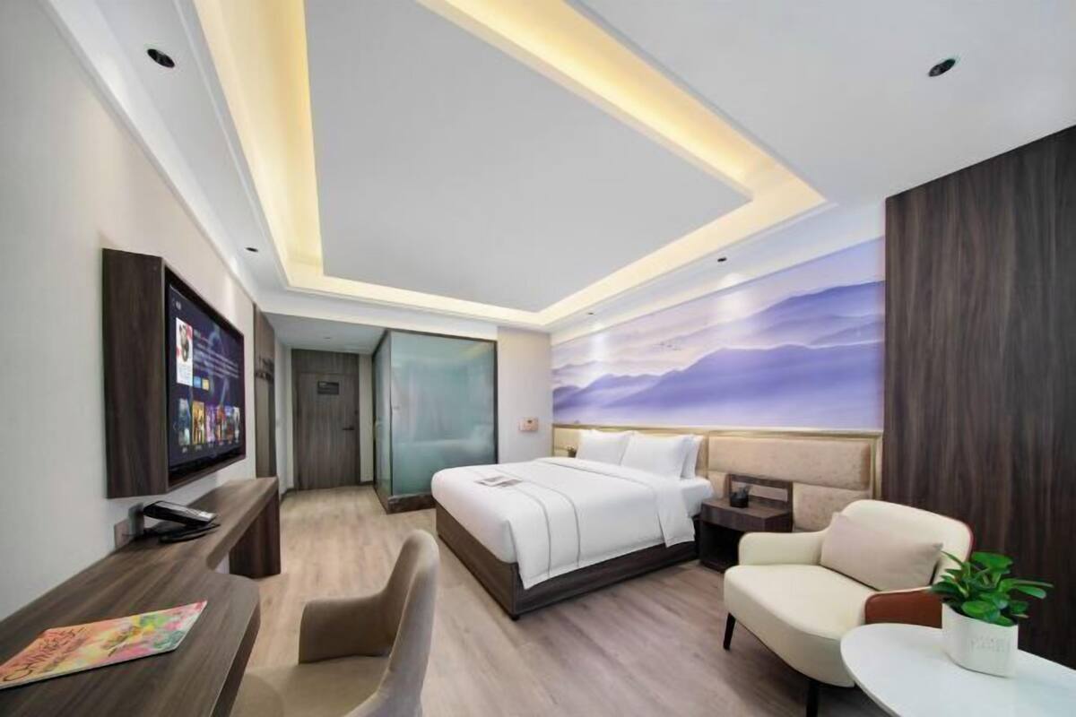 A modern hotel room with a bed, seating area, and a TV on the wall.