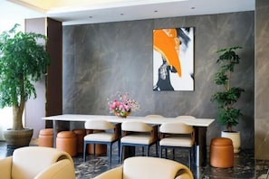 A hotel lobby with a marble floor, a long dining table with chairs, a potted plant, and a large abstract painting on the wall. - Coffey Hotel (Hongyuan)