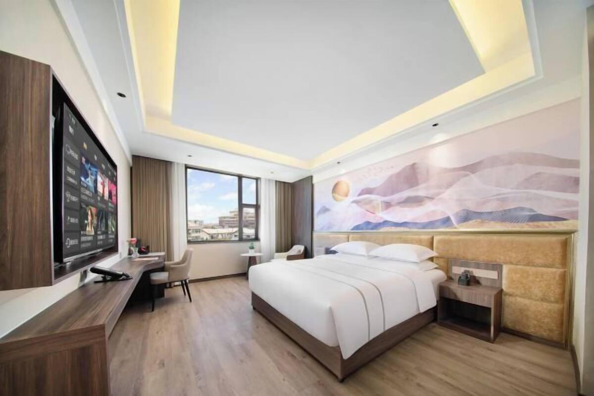 A modern hotel room with a large bed, a desk, a television, and a city view.