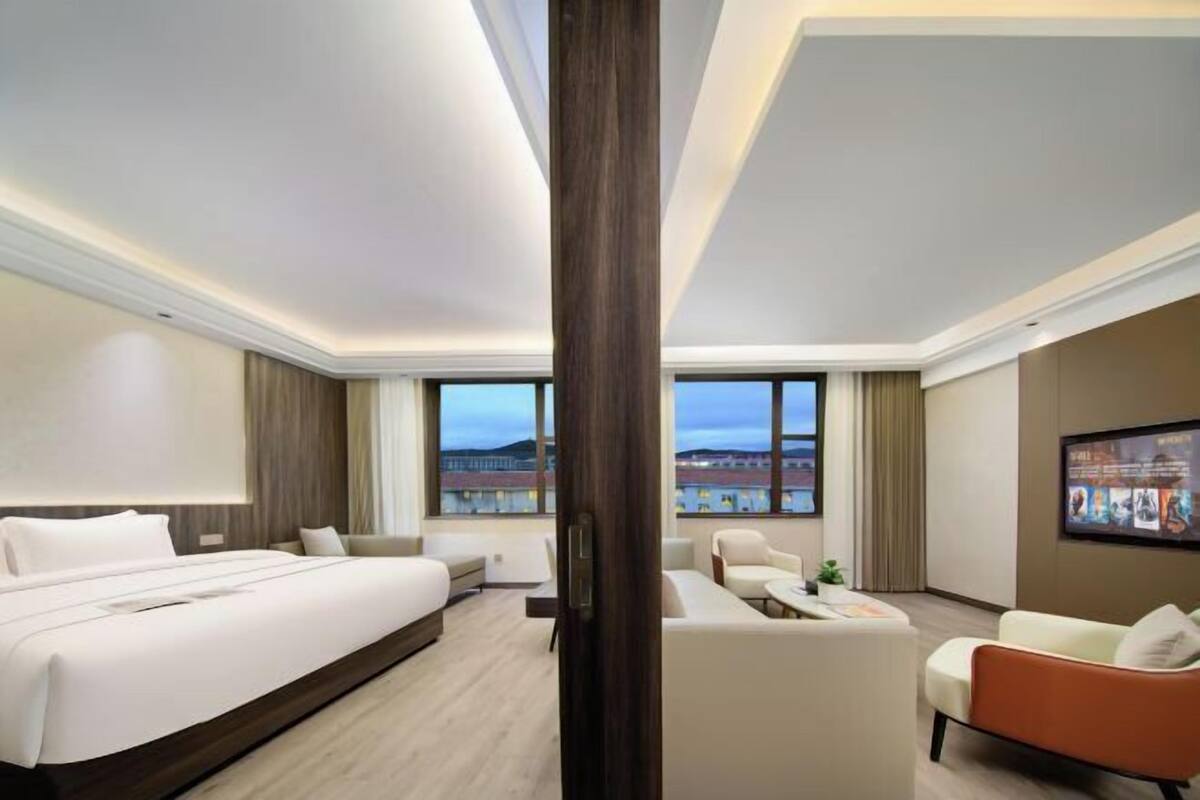 A hotel room with a large bed, a sofa, a chair, and a TV on the wall.