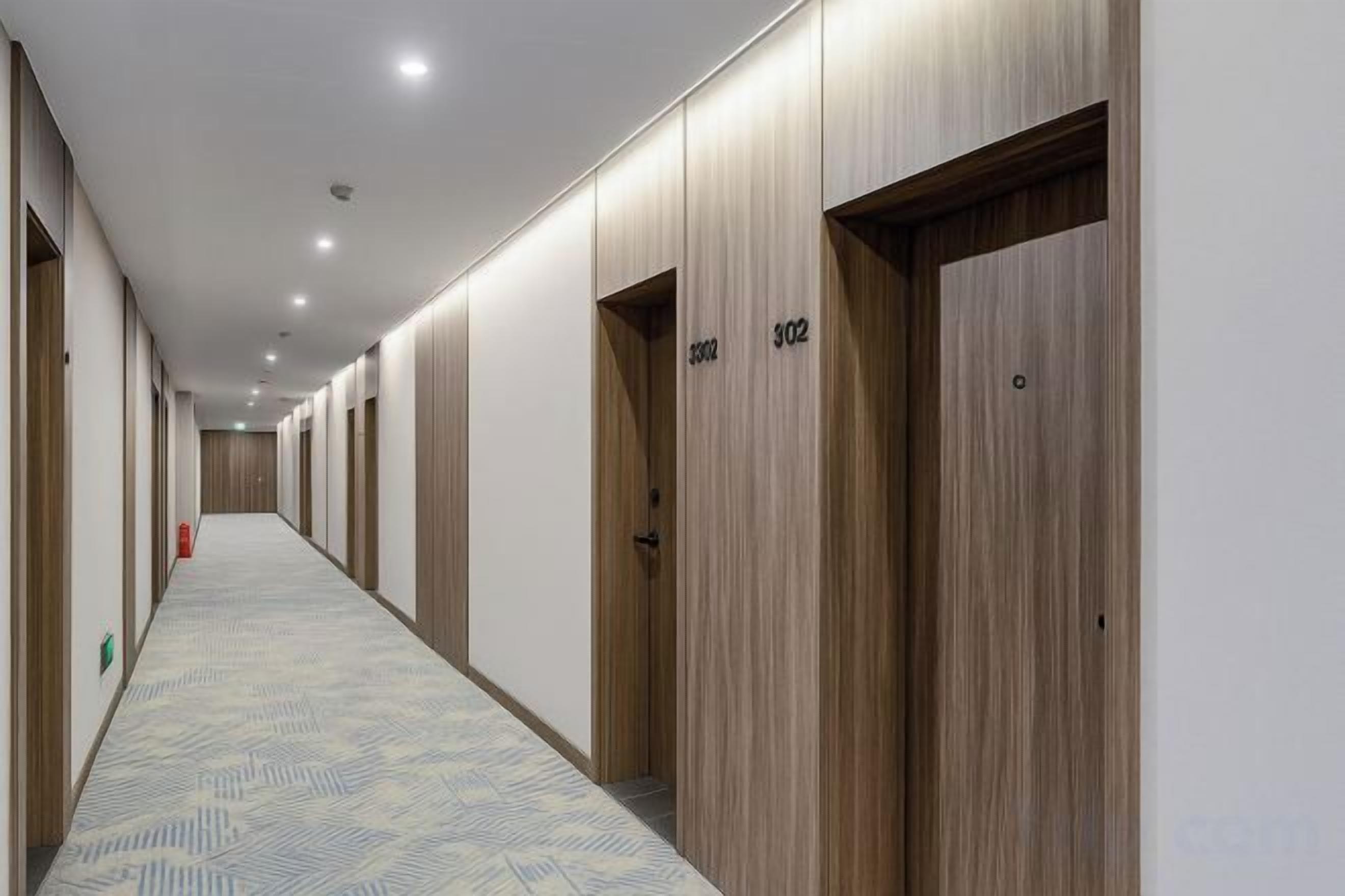 Un couloir d’hôtel avec des portes en bois, numérotées 302 et 303, et un tapis à motifs.