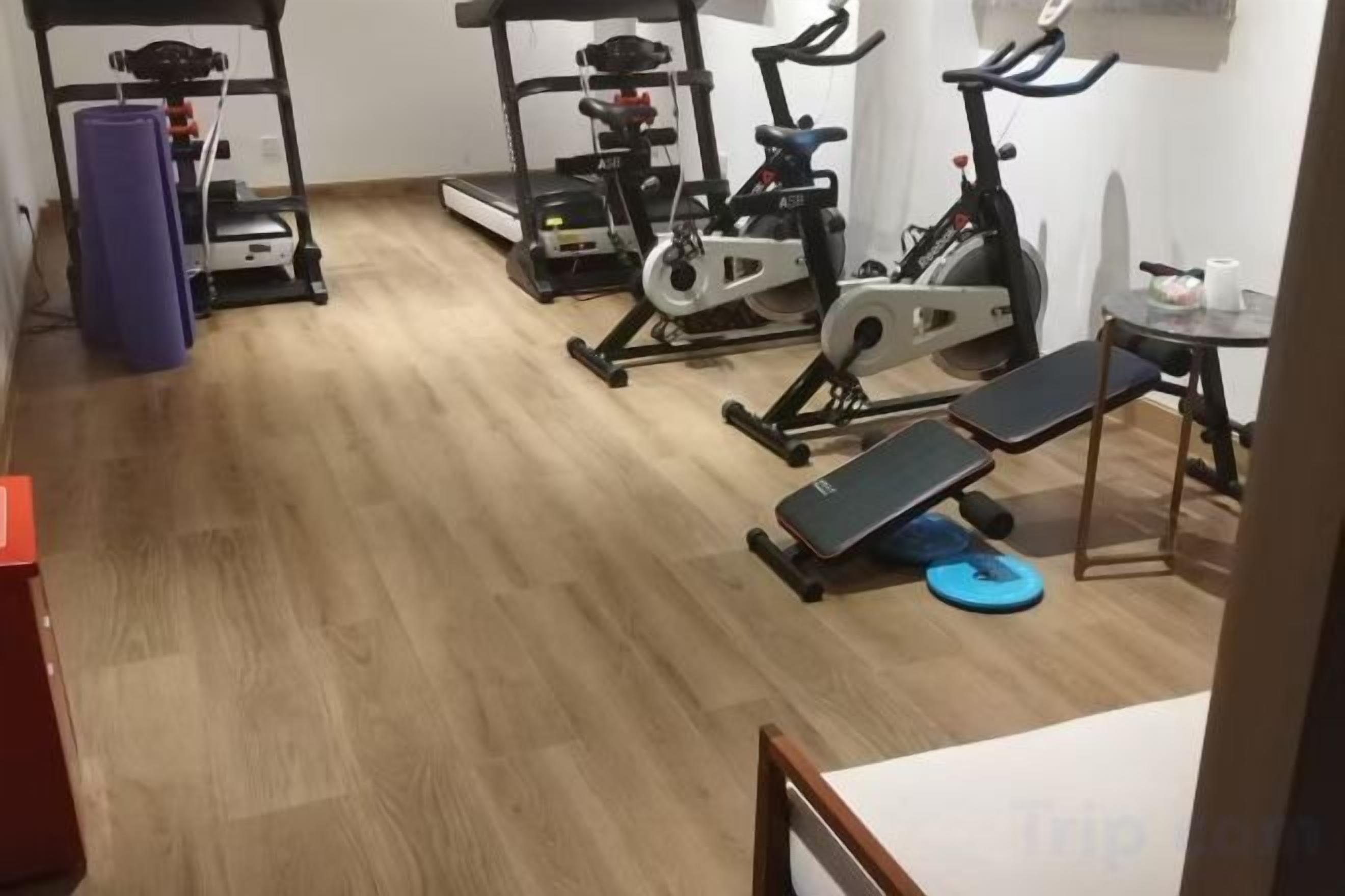 Ein Fitnessraum mit Trainingsgeräten, darunter Laufbänder, Ergometer und eine Bank.