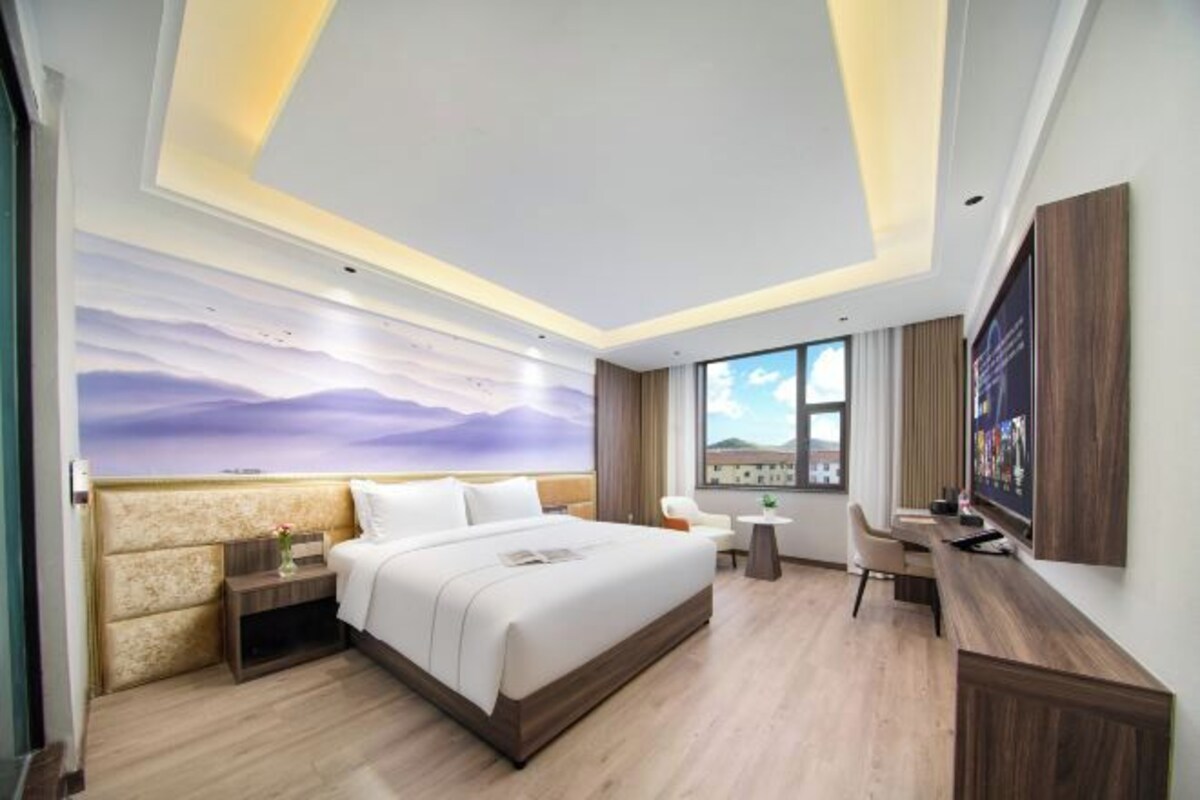 Una habitación de hotel moderna con una cama grande, un escritorio, una silla, una mesita pequeña y un ventanal amplio.