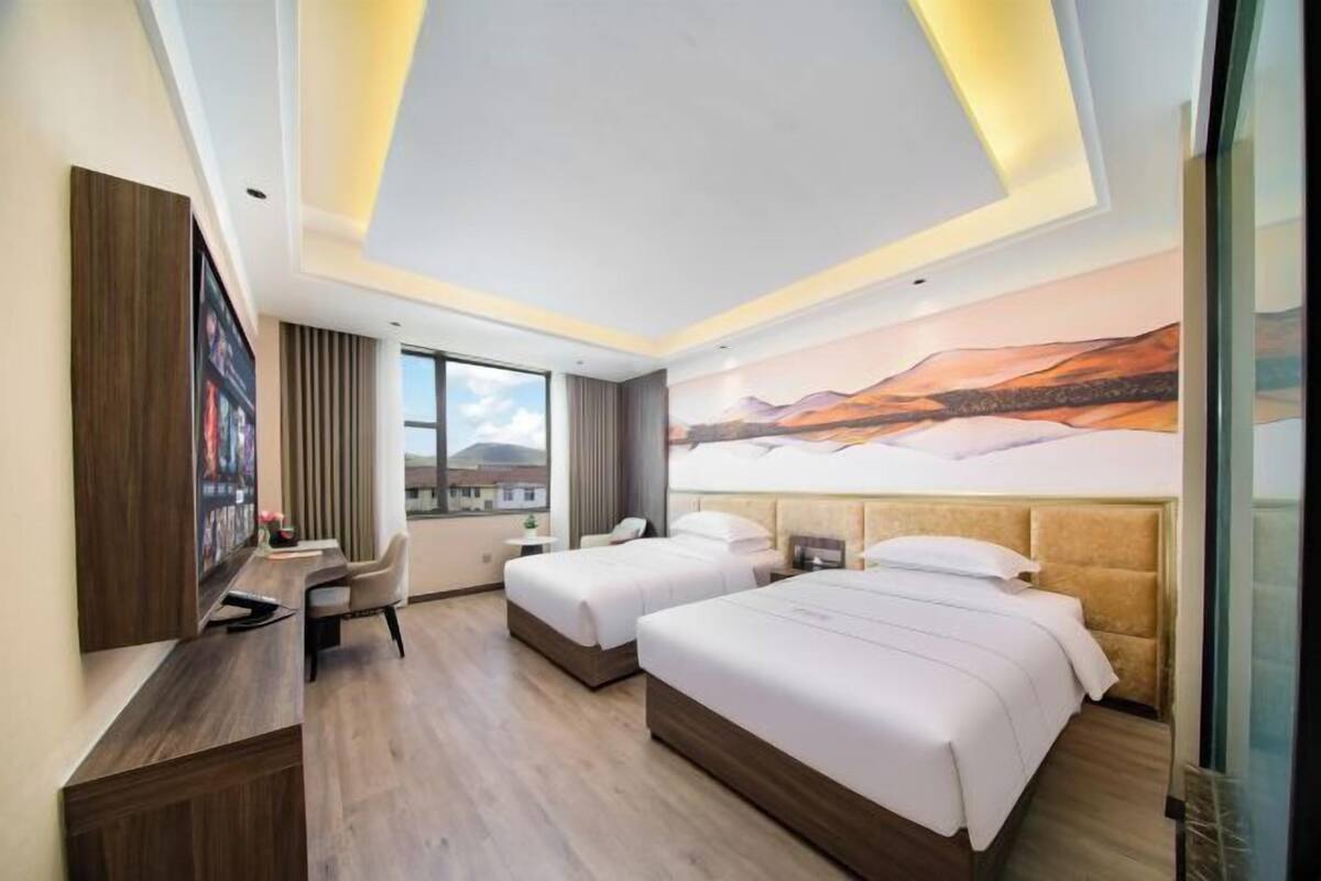 A hotel room with two beds, a desk, and a large window.