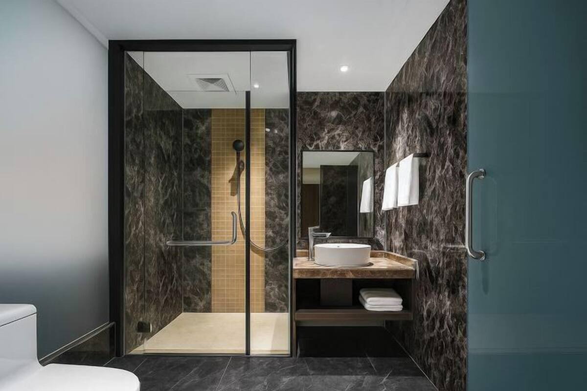 A modern bathroom with a glass-enclosed shower, a marble wall, a sink with a mirror, and a towel rack.
