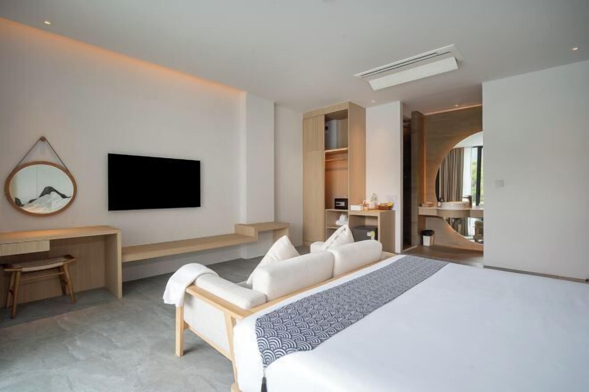A modern hotel room with a bed, a desk, a chair, a TV, and a wardrobe.