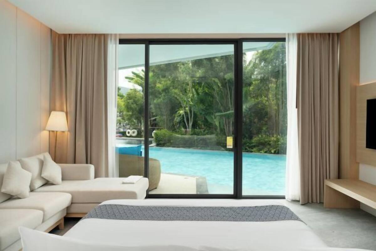 A hotel room with a bed, a sofa, a TV, and a large sliding glass door leading to a pool.