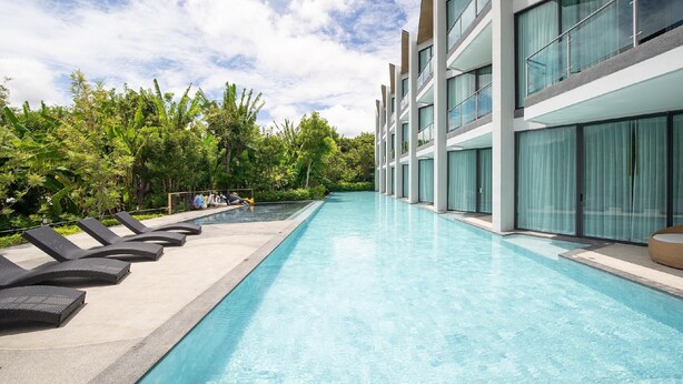 A modern hotel with a long swimming pool, lounge chairs, and lush greenery. - Timberton Resort Khaoyai (Pak Chong)