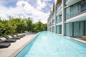 Un hôtel moderne doté d’une longue piscine, de chaises longues et d’une végétation luxuriante.