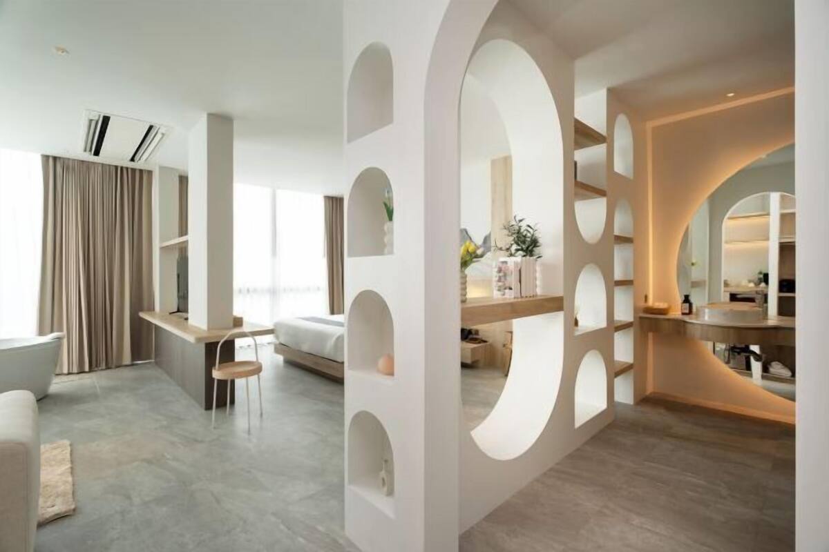 A modern hotel room with a large window, a built-in desk, and a cozy seating area.