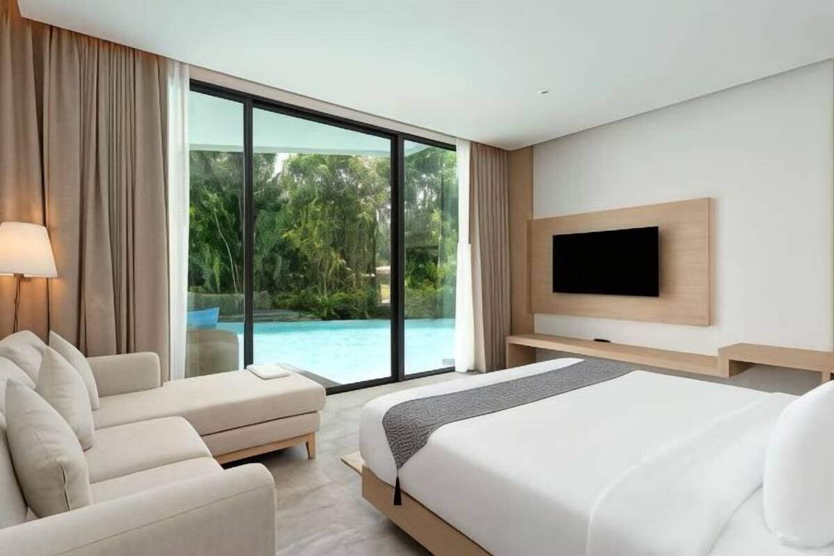 A hotel room with a bed, a sofa, a TV, and a view of a swimming pool.