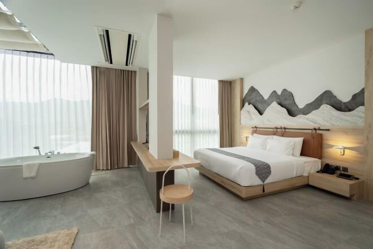 A modern hotel room with a large bed, a bathtub, a desk, and a view of the mountains.
