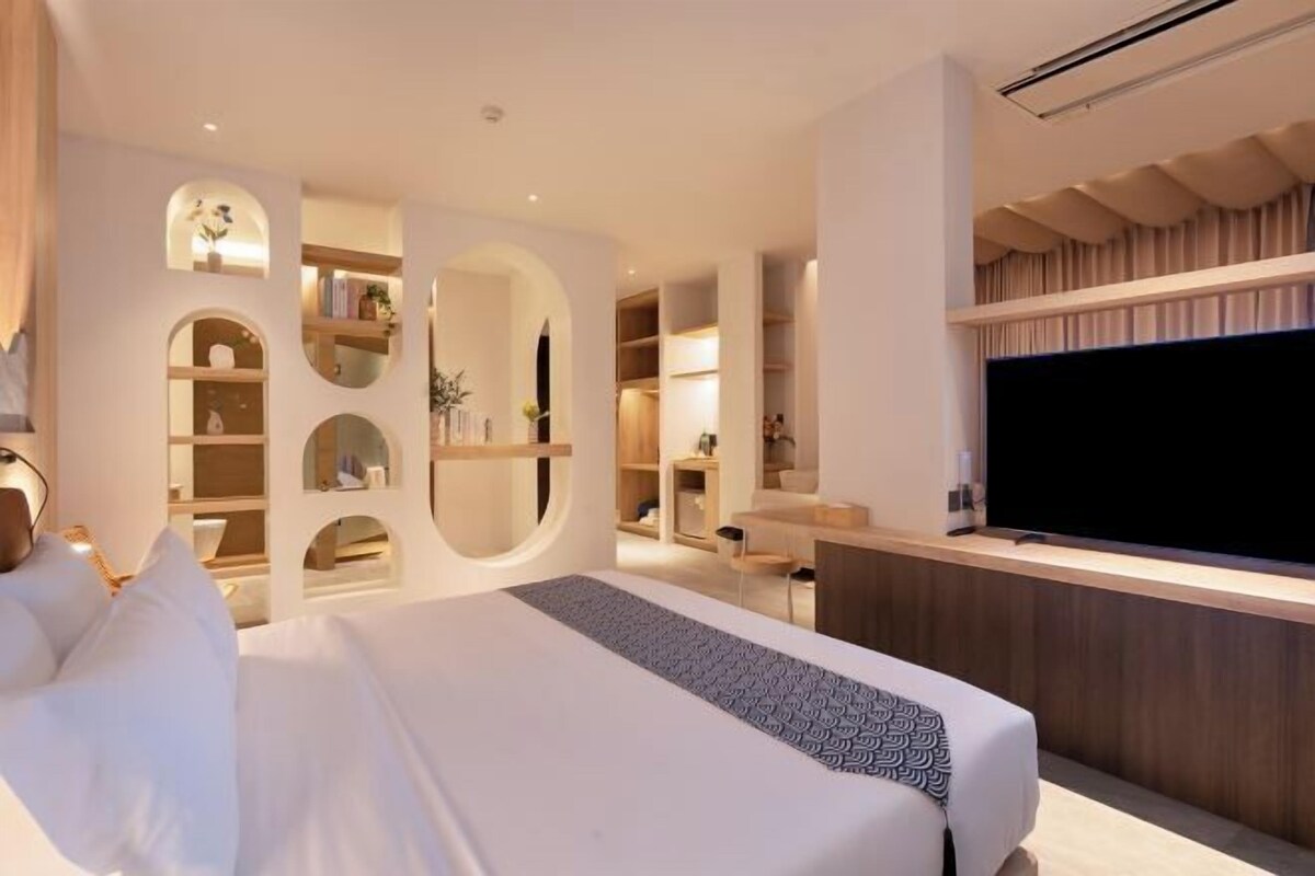 A modern hotel room with a large bed, built-in shelving, a flat-screen TV, and a desk area.