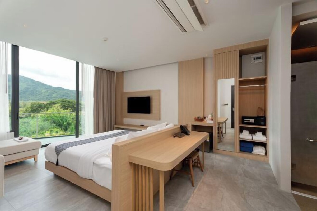 A modern hotel room with a large bed, a desk, a TV, and a wardrobe.