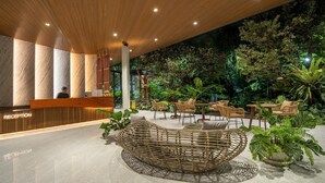 A reception area with a wooden reception desk, a circular wicker seating area, and a lush indoor garden with various plants and seating arrangements. - Timberton Resort Khaoyai (Pak Chong)