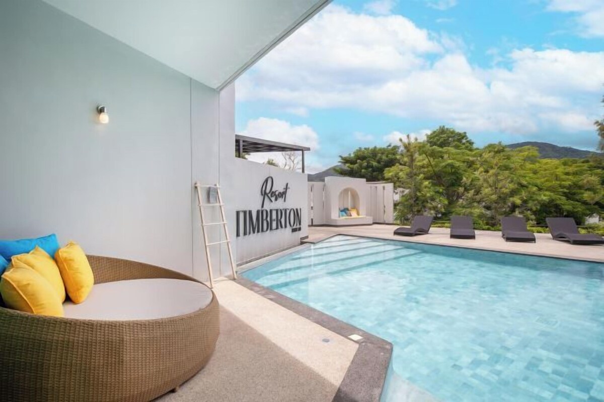 A poolside area with a lounge chair, a small seating area with cushions, and a sign that reads 'Timberton Resort.'