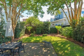 Relax in a serene backyard oasis with a paved patio, table, chairs, and umbrella, surrounded by lush greenery and a peaceful atmosphere.