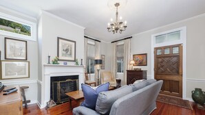 Ein Wohnzimmer mit Kamin, einer Couch, einer Chandelier und gerahmten Kunstwerken an den Wänden.