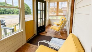 A covered porch with yellow furniture, large windows, and a ceiling fan. - Stunning Cottage across for public Bayshore beach (Grand Marais)