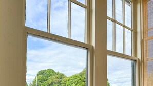 A room with large windows offering a view of a parking lot and trees. - Stunning Cottage across for public Bayshore beach (Grand Marais)