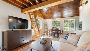 Un soggiorno con soffitto in legno, una TV a schermo piatto, un divano, un tavolino da caffè e un'area pranzo con sedie e tavolo.