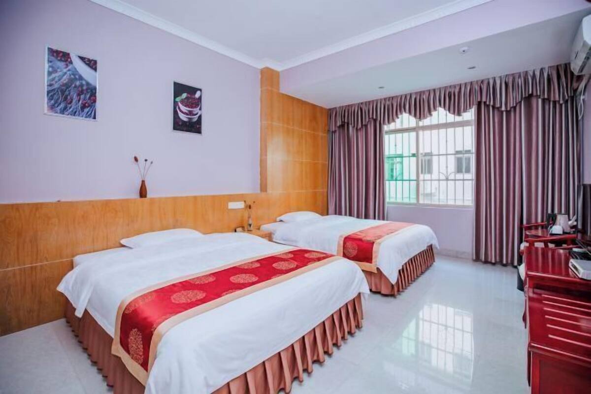A hotel room with two beds, wooden headboard, large window with curtains, and a red desk.
