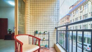 A balcony with a chair, tiled walls, a metal shelf with plants, and a view of a street.