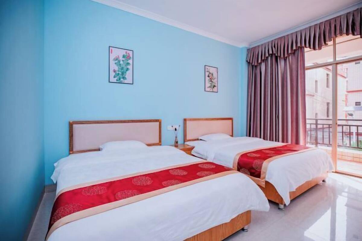A hotel room with two beds, a large window with curtains, and artwork on the walls.