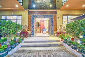 Entrada de hotel con una escalera monumental, plantas en macetas y una zona de recepción.