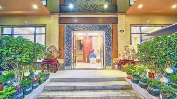 A hotel entrance with a grand staircase leading to a reception area, flanked by potted plants and decorative statues. - Hongdou Lanting Inn (Renhua)