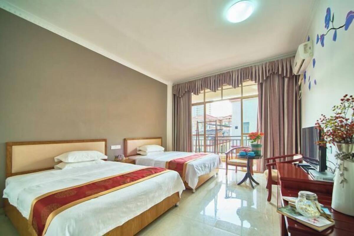 A hotel room with two beds, a desk, a chair, a TV, and a window with curtains.