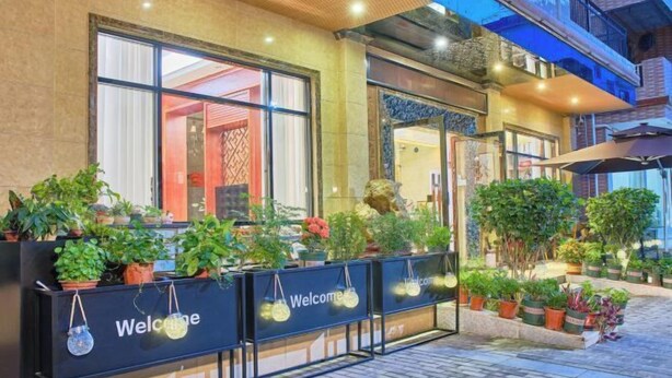 A hotel entrance with a welcoming sign, potted plants, and a tiled pathway.