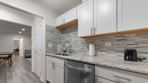 A modern kitchen with white cabinets, a stainless steel dishwasher, and a tiled backsplash.