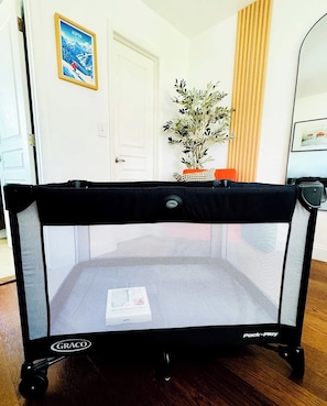 Ein Graco Pack n Play Reisebett in einem Zimmer mit einer weißen Tür, einem gerahmten Bild an der Wand und einem Topf mit Pflanze.