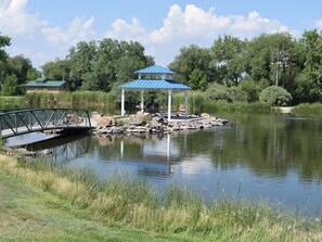 A gazebo on a lakeside with a bridge, surrounded by greenery and trees. - Themed Bedrooms, Movie Room & Firepit Yard (Westminster)