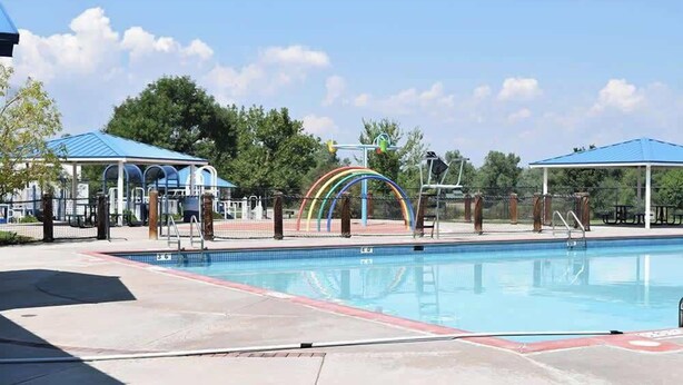 A swimming pool with a rainbow-colored structure, covered seating areas, and trees in the background. - Themed Bedrooms, Movie Room & Firepit Yard (Westminster)