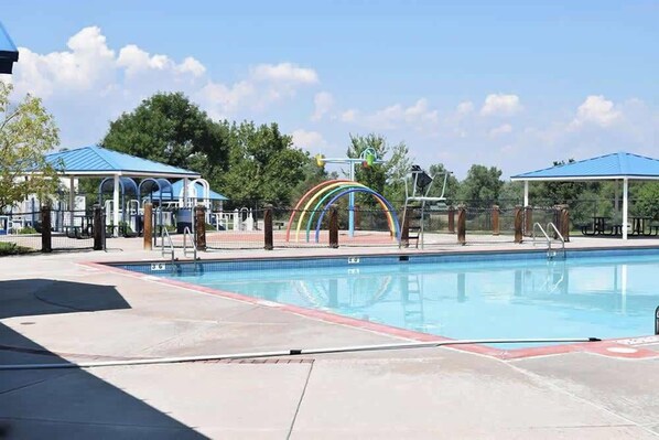 A swimming pool with a rainbow-colored structure, covered seating areas, and trees in the background. - Themed Bedrooms, Movie Room & Firepit Yard (Westminster)