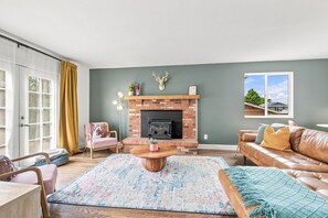 A living room with a fireplace, a sofa, a coffee table, and a view of the outdoors.