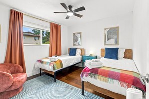 Un dormitorio con dos camas, un ventilador de techo y una ventana con cortinas.